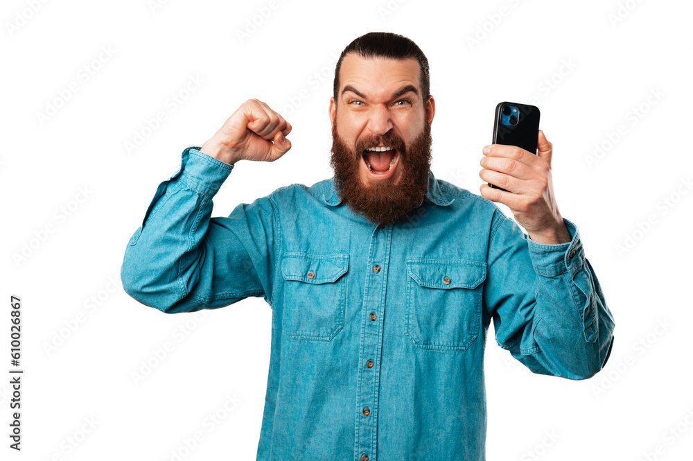 Excited screaming bearded man is making the winner gesture with his phone. Excited screaming bearded man is making the winner gesture with his phone.