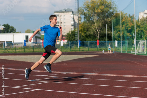 Young teen boy running on the running track at the stadium outdoors
