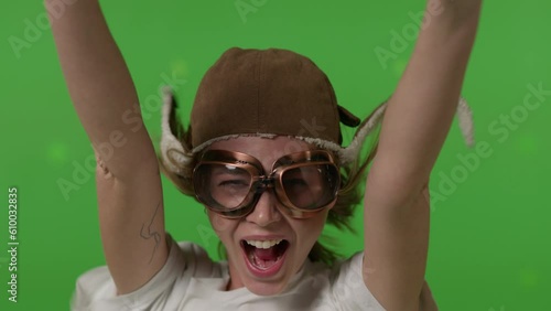 Close-up of a girl's face in a retro pilot's hat blown by a strong wind on Green screen background, chroma key.
