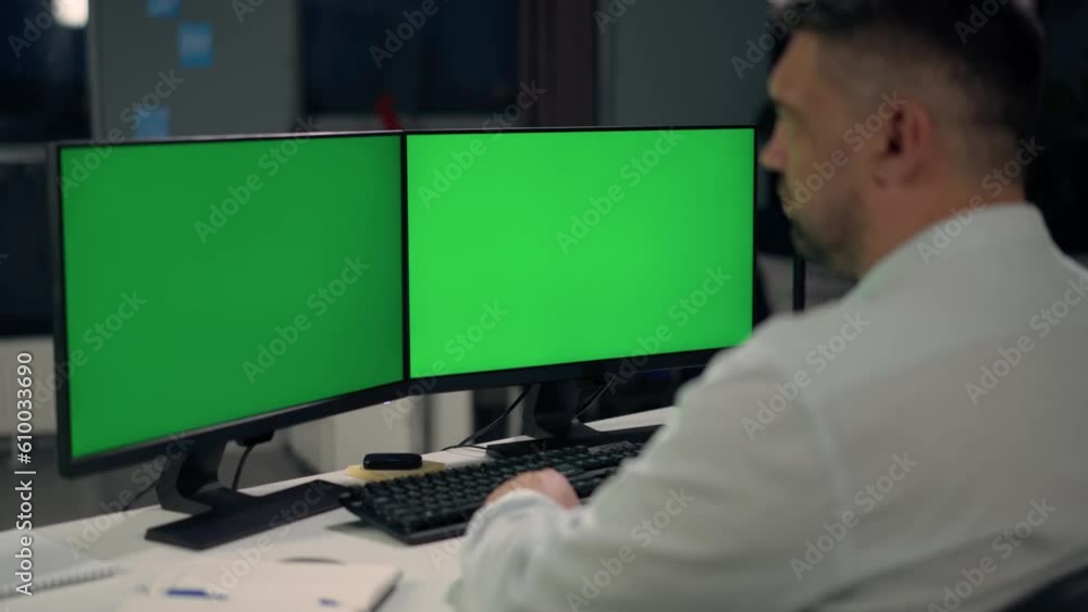 Man Uses Desktop Computer With Two Green Screen Mock Ups Working at Home. Close Up of Monitors With Green Screen On Desktop Man Uses Desktop Computer With Two Green Screen Mock Ups Working at Home. Close Up of Monitors With Green Screen On Desktop