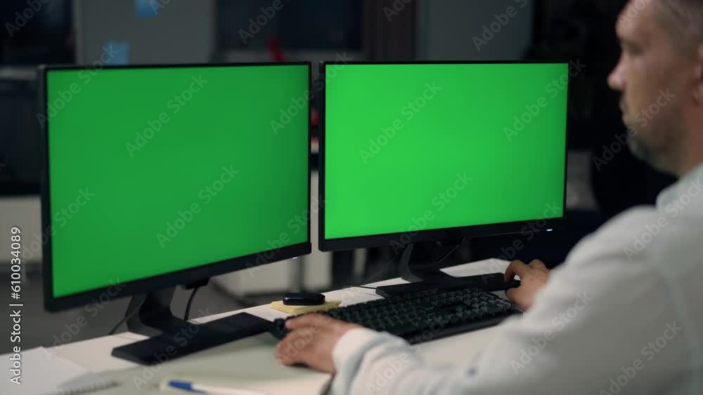 Man Uses Desktop Computer With Two Green Screen Mock Ups Working at Home. Close Up of Monitors With Green Screen On Desktop Man Uses Desktop Computer With Two Green Screen Mock Ups Working at Home. Close Up of Monitors With Green Screen On Desktop