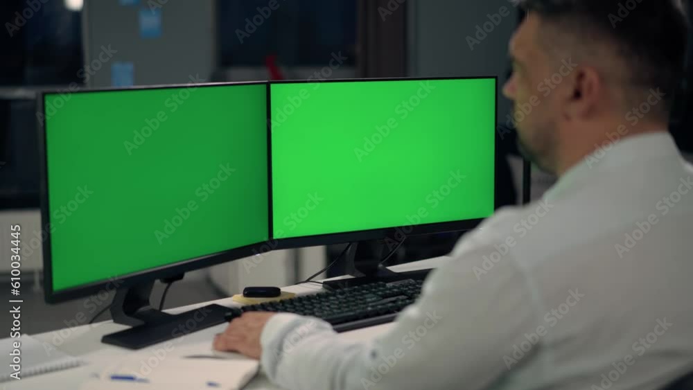 Man Uses Desktop Computer With Two Green Screen Mock Ups Working at Office Man Uses Desktop Computer With Two Green Screen Mock Ups Working at Office