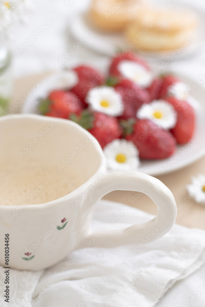A plate of strawberries is decorated with white daisies. Berries with vitamins and a cup of aromatic coffee A plate of strawberries is decorated with white daisies. Berries with vitamins and a cup of aromatic coffee