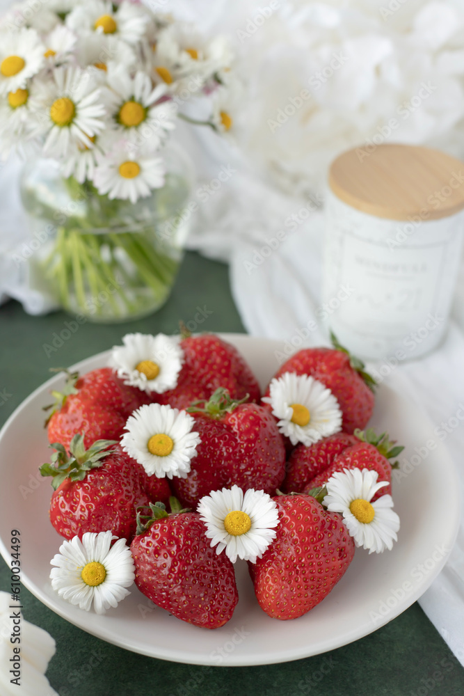 A plate of strawberries is decorated with white daisies. Berries with vitamins