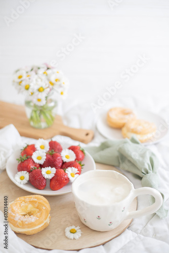 A plate of strawberries is decorated with white daisies. Berries with vitamins and a cup of aromatic coffee