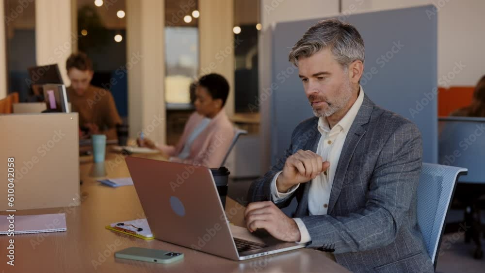 Good looking senior businessman in formal clothes typing at the laptop and smiling of his success. Optimistic Male manager with a Focused Gaze on Laptop Screen. Outdoors. Business people concept. Good looking senior businessman in formal clothes typing at the laptop and smiling of his success. Optimistic Male manager with a Focused Gaze on Laptop Screen. Outdoors. Business people concept.