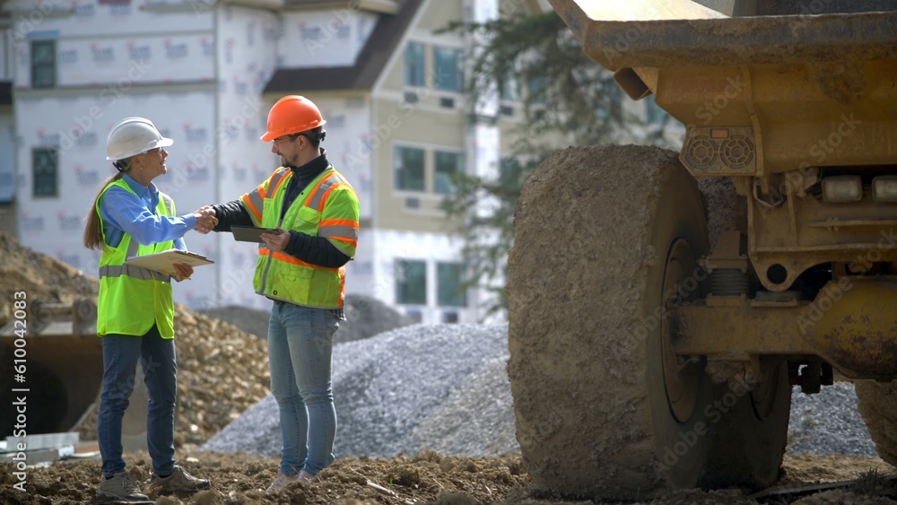 Woman engineer architect shakes hands with construction project foreman in front of a building and next to a dump truck. Woman engineer architect shakes hands with construction project foreman in front of a building and next to a dump truck.