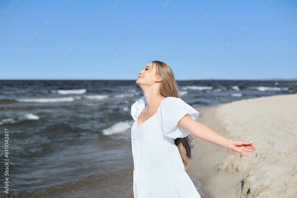 Happy smiling beautiful woman is on the ocean beach in a white summer dress, open arms. Happy smiling beautiful woman is on the ocean beach in a white summer dress, open arms.