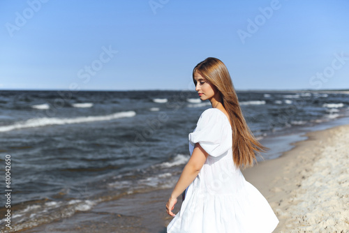 Happy, beautiful woman on the ocean beach standing in a white summer dress. Portrait.