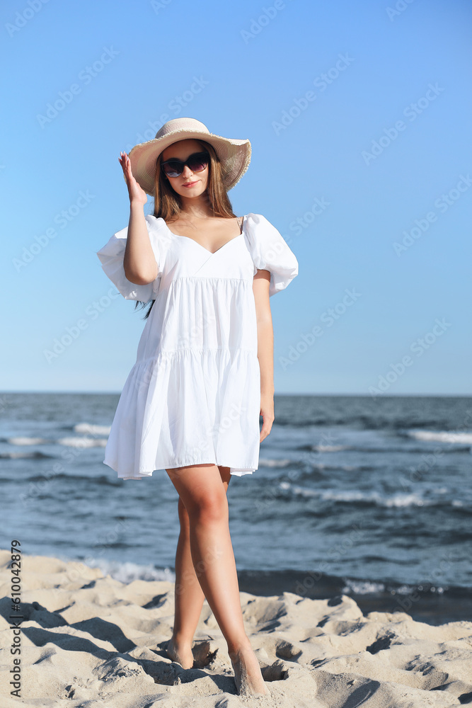 Happy smiling blonde woman is posing on the ocean beach with sunglasses and a hat. Happy smiling blonde woman is posing on the ocean beach with sunglasses and a hat.