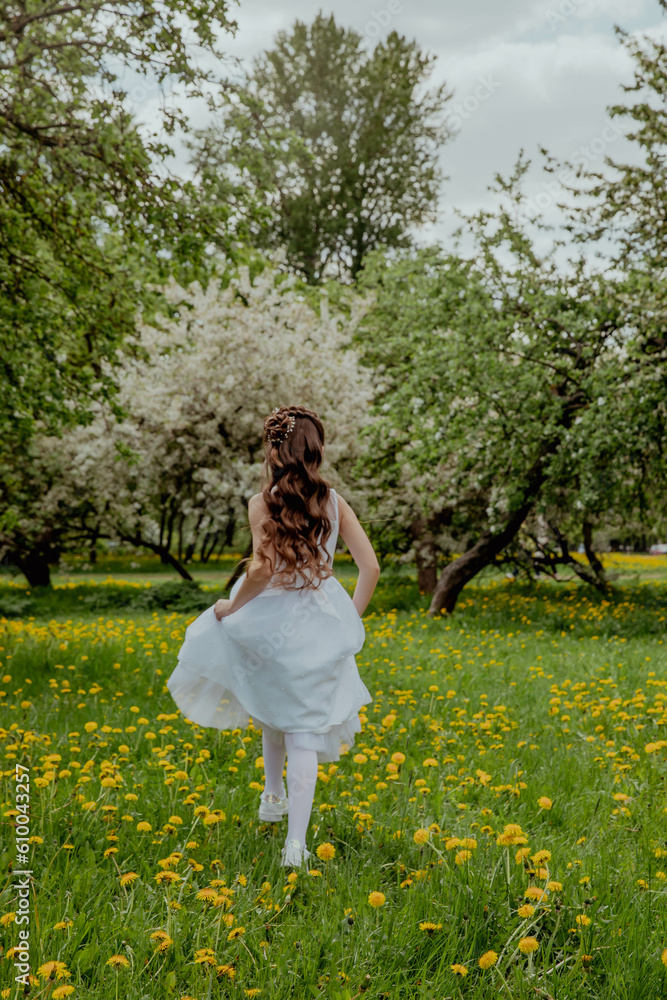 Fototapeta premium Girl in white dress running through a blossoming apple orchard