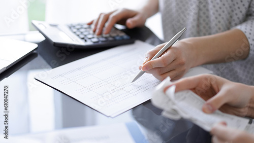 Woman accountant using a calculator and laptop computer while counting taxes with a client or colleague. Business audit team.