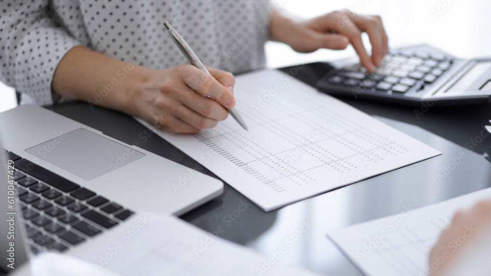 Woman accountant using a calculator and laptop computer while counting taxes for a client. Business audit concepts.