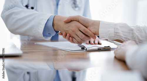 Doctor and patient shaking hands above the wooden table in clinic. Medicine concept.