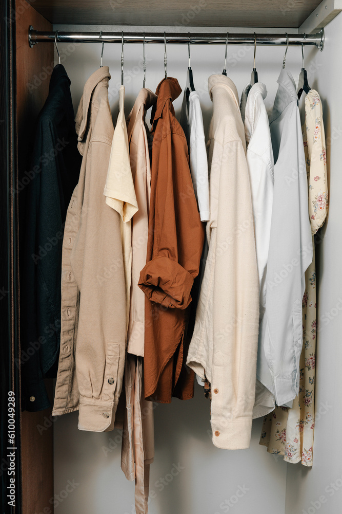 Vertical photo of colorful shirts, t-shirts and dresses on hangers in closet. The concept of changing the wardrobe, storing things and choosing clothes