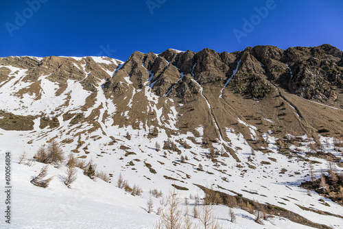 Принти на полотні A scenic view of a rocky mountain cliff with some snow under a majestic blue sky