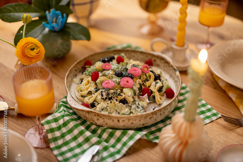 Tasty pasta with spinach and berries decorated with edible flowers on a plate for sharing at beautifuly served dining table photo