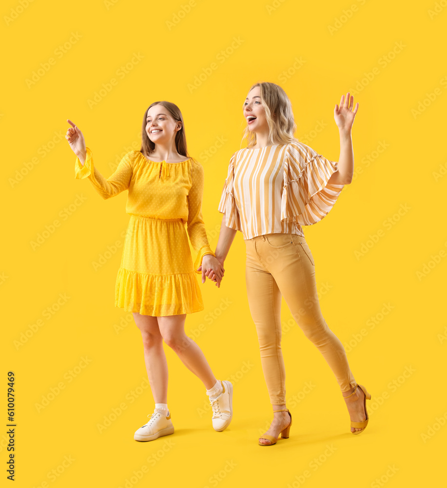 Fototapeta premium Young sisters holding hands on yellow background