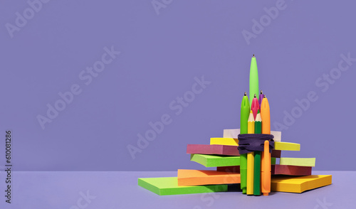 Stationery rocket out of pens on desk on top of pile of sticky notes. purple background. back to school or education and creativity concept. Success achievement. Team work ideas and leadership