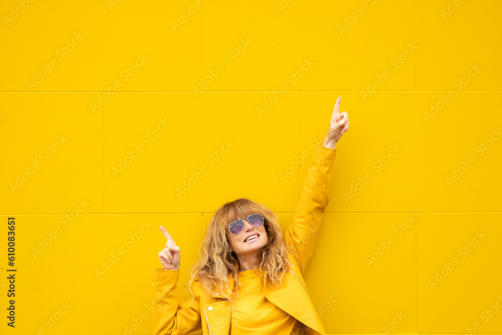 middle aged woman on yellow wall with outstretched arm of happiness