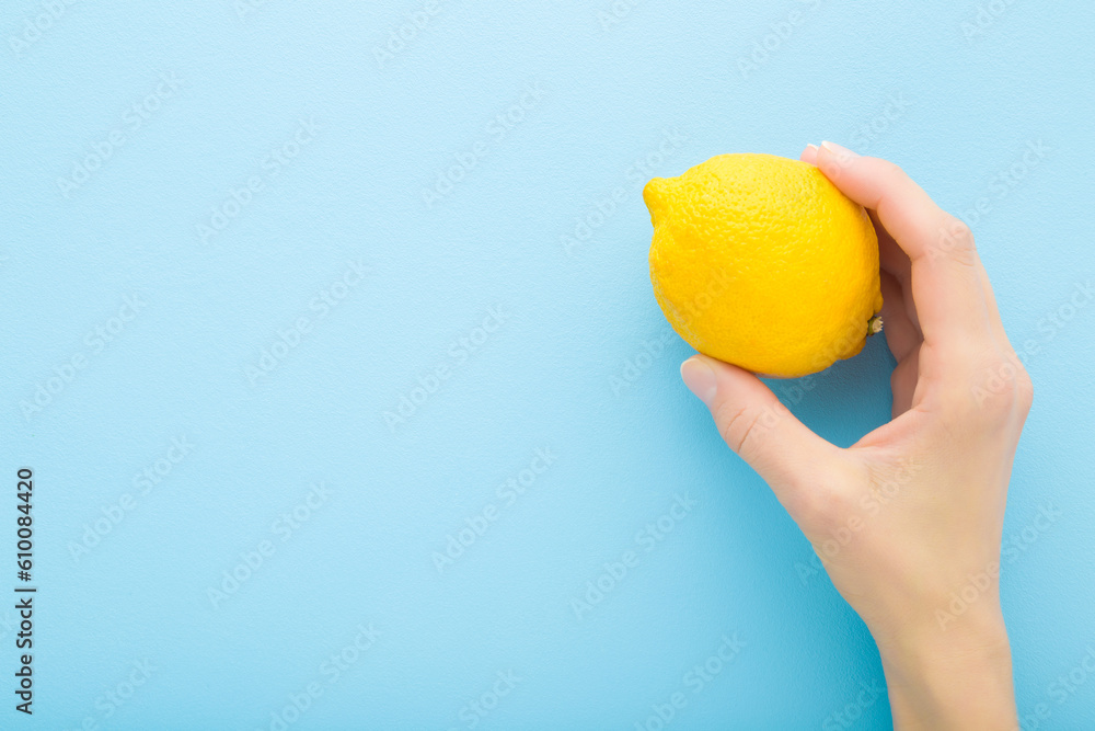 Young adult woman hand holding yellow lemon on light blue table background. Pastel color. Fresh fruit. Closeup. Empty place for text. Top down view. Young adult woman hand holding yellow lemon on light blue table background. Pastel color. Fresh fruit. Closeup. Empty place for text. Top down view.