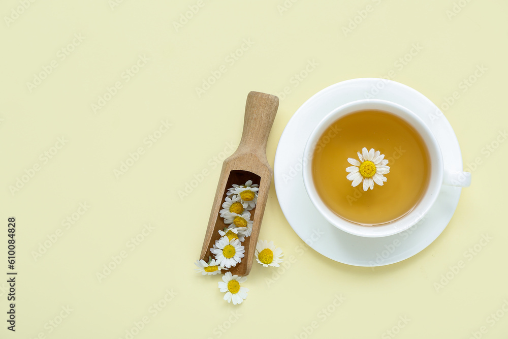 Cup of hot chamomile tea with scoop on pale yellow background Cup of hot chamomile tea with scoop on pale yellow background