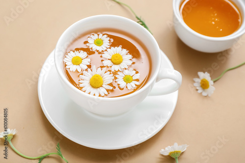 Cup of hot chamomile tea with honey on beige background