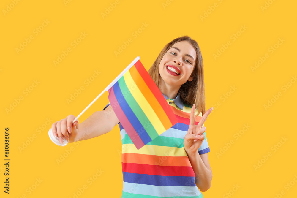 Young woman with LGBT flag showing victory gesture on yellow background Young woman with LGBT flag showing victory gesture on yellow background