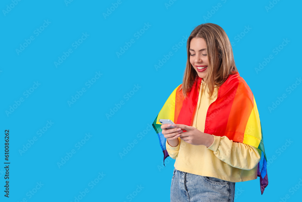 Happy young woman with LGBT flag using mobile phone on blue background Happy young woman with LGBT flag using mobile phone on blue background