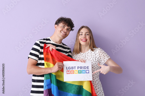Young couple holding paper with text LGBT PRIDE MONTH and flag on lilac background