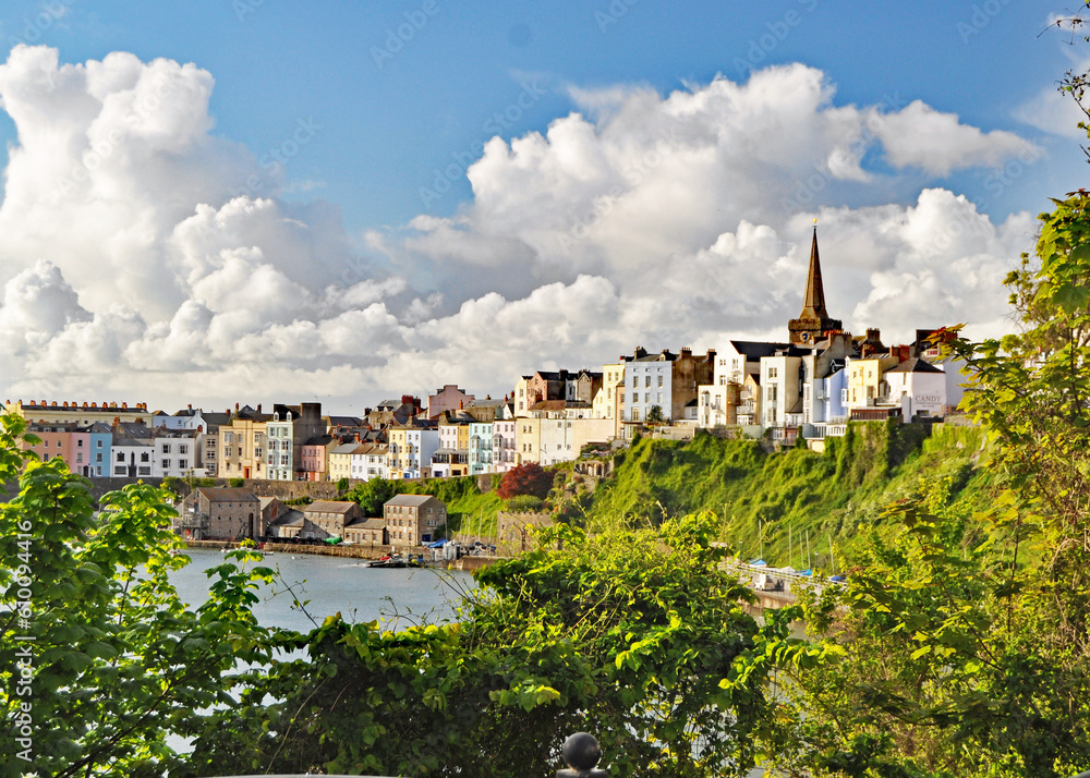 A beautiful panorama framed by green trees and bushes of the pretty resort town of Tenby in Wales with interesting white clouds