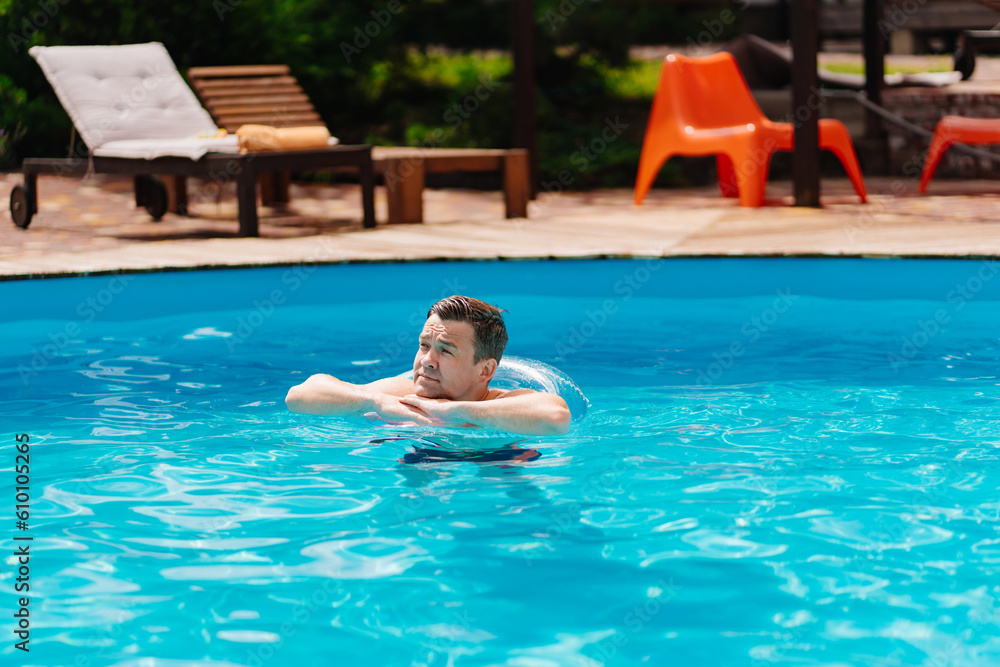 Portrait of a cheerful middle-aged man in the pool with inflatable lifebuoy.