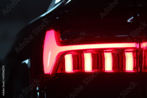 Car tail lights bright in the night/ Sports car rear profile background image, studio light. Car detail. LED taillights in hybrid sedan. With copy space. Neon lights in the night. Car in a dark city.