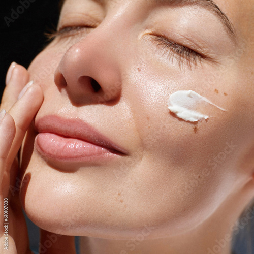 Skincare daily treatment. Beauty close up portrait of young woman with a healthy skin is applying a facial care product. Cream smear.