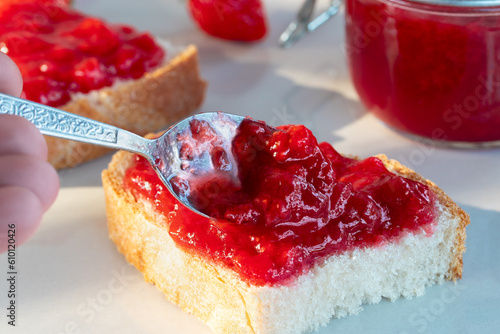 Spreading strawberry jam on a piece of wheat bread