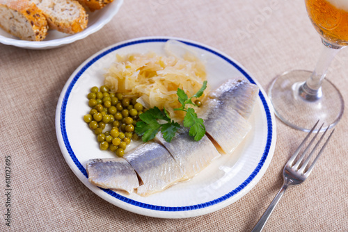 Light salted herring with pickled cabbage and green peas dished up in a plate on the laid table