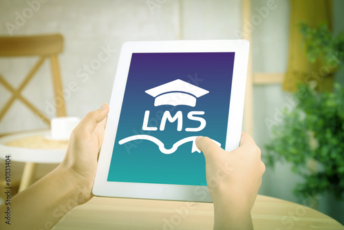 Learning management system. Woman using tablet at table, closeup. Open book and graduate cap icons with abbreviation LMS on screen photo