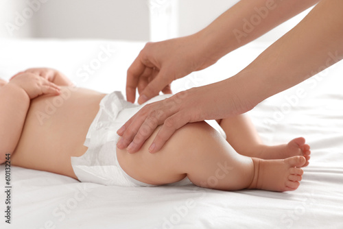 Mother changing her newborn baby's diaper on bed at home, closeup