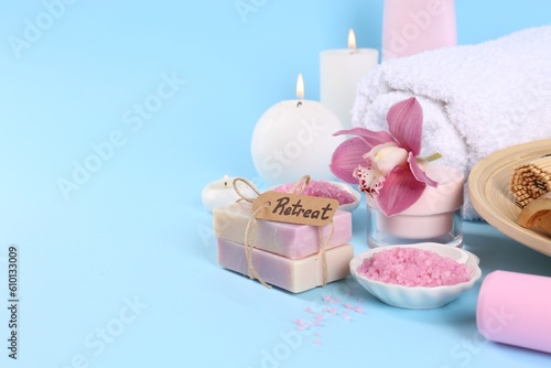 Retreat concept. Burning candles, orchid flower and different spa products on light blue background. Space for text
