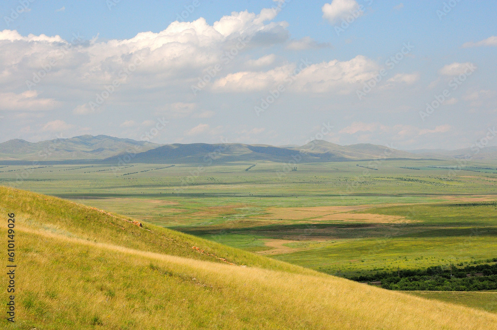View of the picturesque endless steppe from the top of a high hill and a mountain range on the horizon on a sunny summer day. View of the picturesque endless steppe from the top of a high hill and a mountain range on the horizon on a sunny summer day.