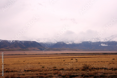 Thunderclouds cover the snow-capped peaks of high mountains and the dry autumn steppe.