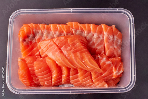 Sliced fresh salmon prepared and arranged in a clear plastic food box isolated on black background, packaging food for take away.