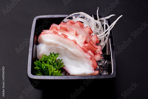 Sliced tako sashimi and radish on ice in a black plate isolated on black background. Sliced boiled squid, popular Japanese food photo