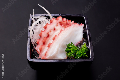 Sliced tako sashimi and radish on ice in a black plate isolated on black background. Sliced boiled squid, popular Japanese food