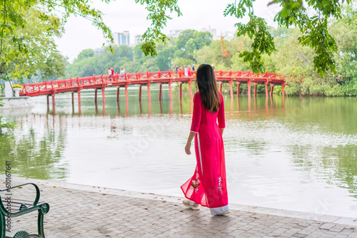 Young Asian woman tourist wearing Ao Dai (traditional Vietnamese dress) sightseeing at the Red Bridge in Hoan Kiem Lake, Hanoi, Vietnam. Copy space photo
