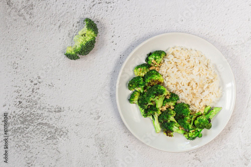 Healthy vegan food stir fried broccoli garlic and brown rice has spoon isolated on white slate background.
