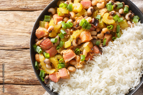 Hoppin John of black-eyed peas, bacon, sausages, vegetables and scallions with rice closeup on the plate on the wooden table. Horizontal top view from above