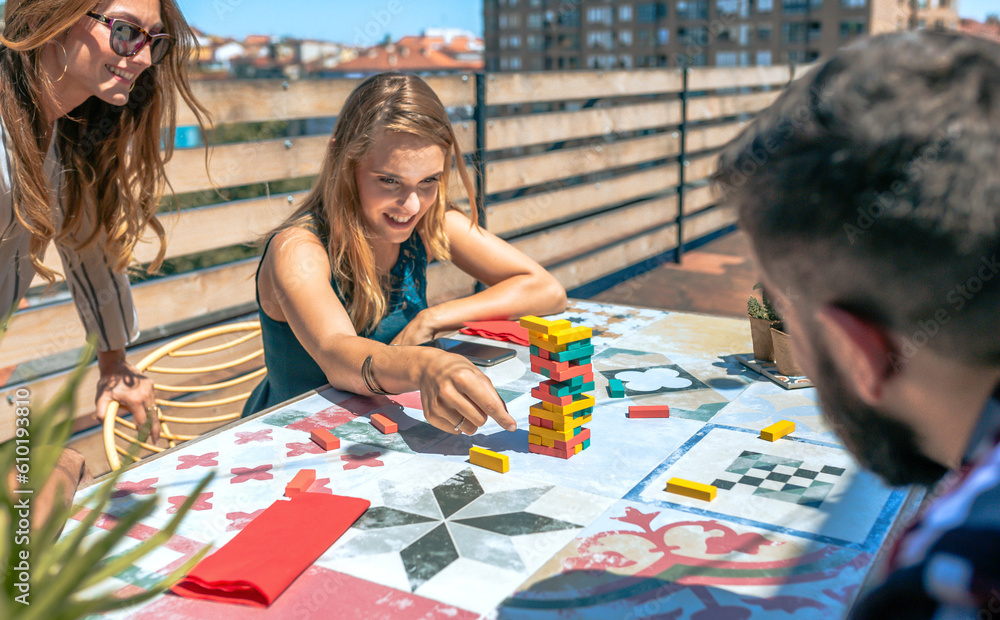 Fototapeta premium Woman looking jenga game piece next to colleagues on terrace