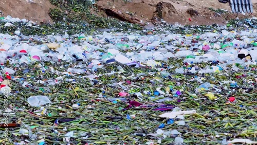 Waves pushing floating plastic trash and lilies to a tropical beach