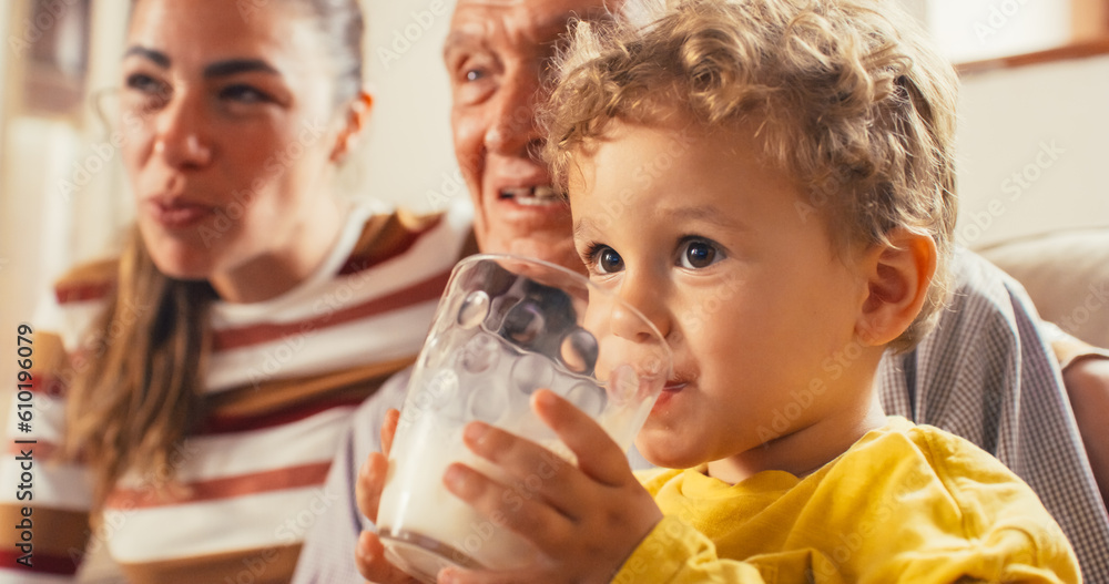 Portrait of Kid Watching TV with his Family While Drinking Milk in the Living Room. His Mother and Grandfather Talking to Him. Cute Toddler Getting Important Nutriments for his Growth and Health Portrait of Kid Watching TV with his Family While Drinking Milk in the Living Room. His Mother and Grandfather Talking to Him. Cute Toddler Getting Important Nutriments for his Growth and Health
